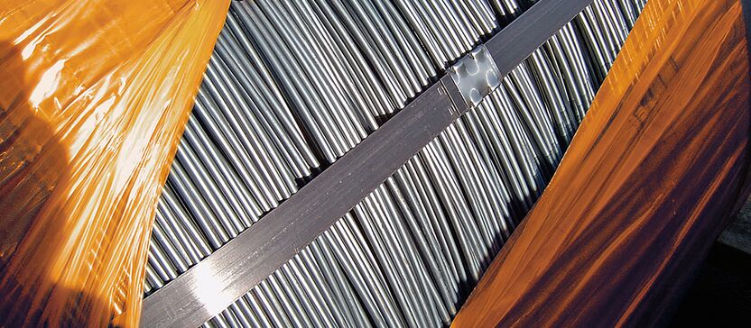 Stahlstangen vollständig verpackt in BioCor® Korrosionsschutzfolie. Zwei überlappende Folien werden von einer Person auseinandergezogen und geben den Bick auf die Stahlstangen frei.